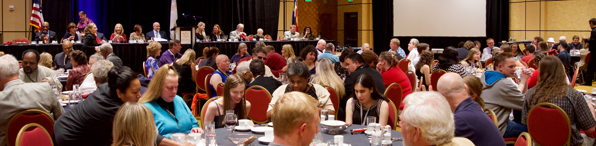 A room full of NFB members at banquet tables smiling and clapping